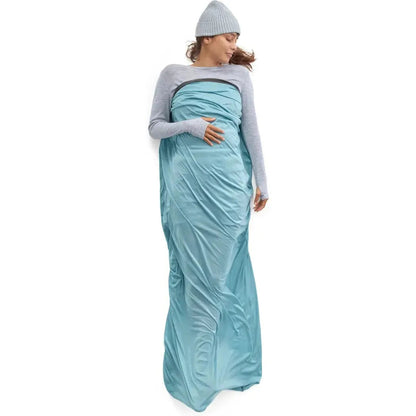 A woman wearing a gray beanie stands against a white background in the Sea To Summit Comfort Blend Sleeping Bag Liner - Rectangular.