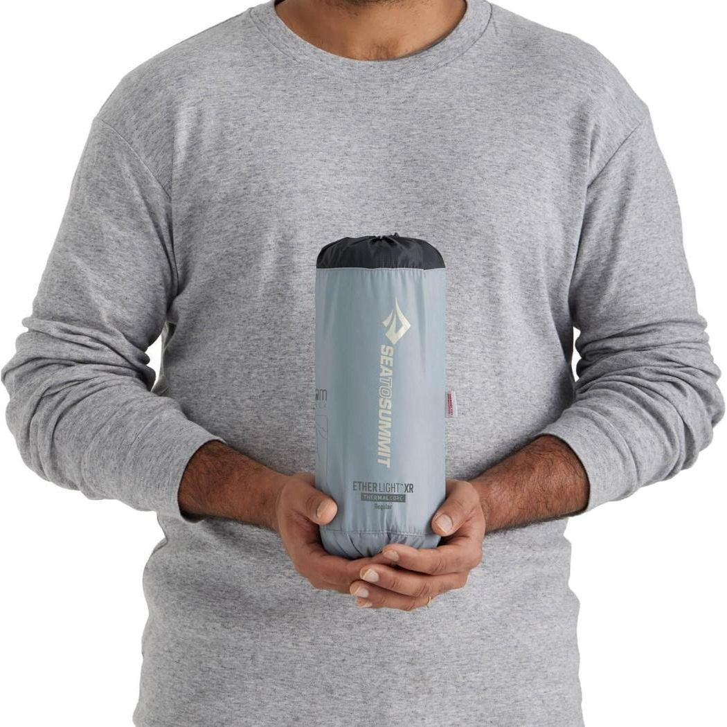 A man in a gray sweatshirt holds the Sea To Summit Ether Light XR Insulated ASC Mat against a white background.