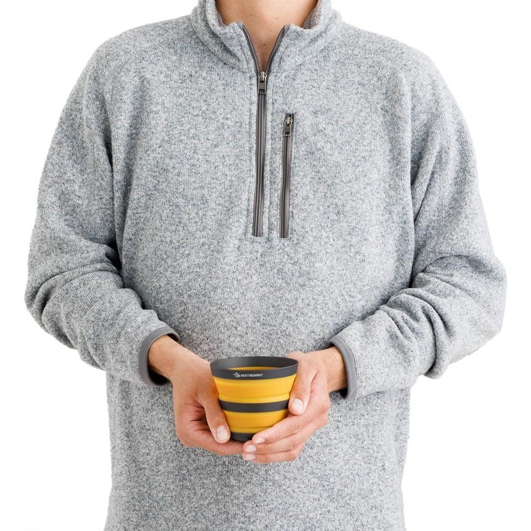 A person wearing a gray fleece holds the Sea To Summit Frontier UL Collapsible Cup in Bone White against a white background.