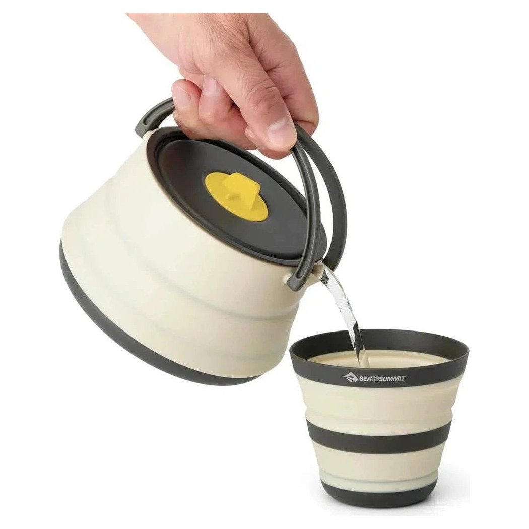 A hand pours from a Sea To Summit Frontier UL Collapsible Kettle into a matching collapsible cup against a white background.