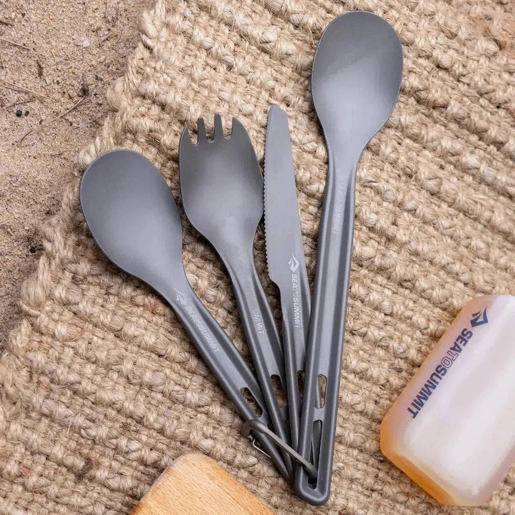 A top-down view of the Sea To Summit Frontier UL Cutlery Set - [2 Piece] Spork and Knife in Charcoal/Graphite on a woven mat with a Sea To Summit bottle nearby.