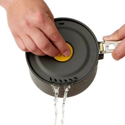 A hand presses the yellow button on the Sea To Summit Frontier UL Pot - 1.3L as water drains from the bottom, shown from a top-down angle.