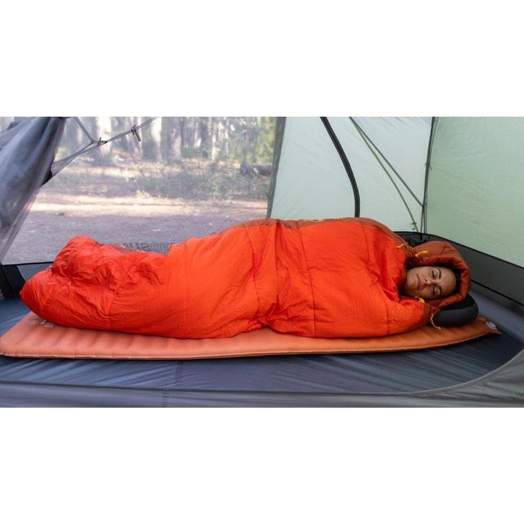A woman lies in a Sea To Summit Hamelin Women's Synthetic Sleeping Bag inside a tent with a forest background.