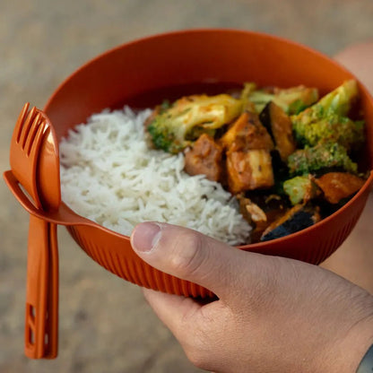 A hand holds the orange Sea To Summit Horizon Bowl - L with rice and veggies, showing the foldable fork on the side.