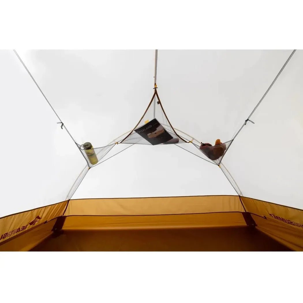 Inside view of the Sea To Summit Ikos Evo Tent showing the interior mesh storage pockets with a book and water bottle against a cloudy sky.