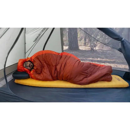 A person sleeps in a Sea To Summit Pursuit Plus SI Mat inside a tent with a forest background.
