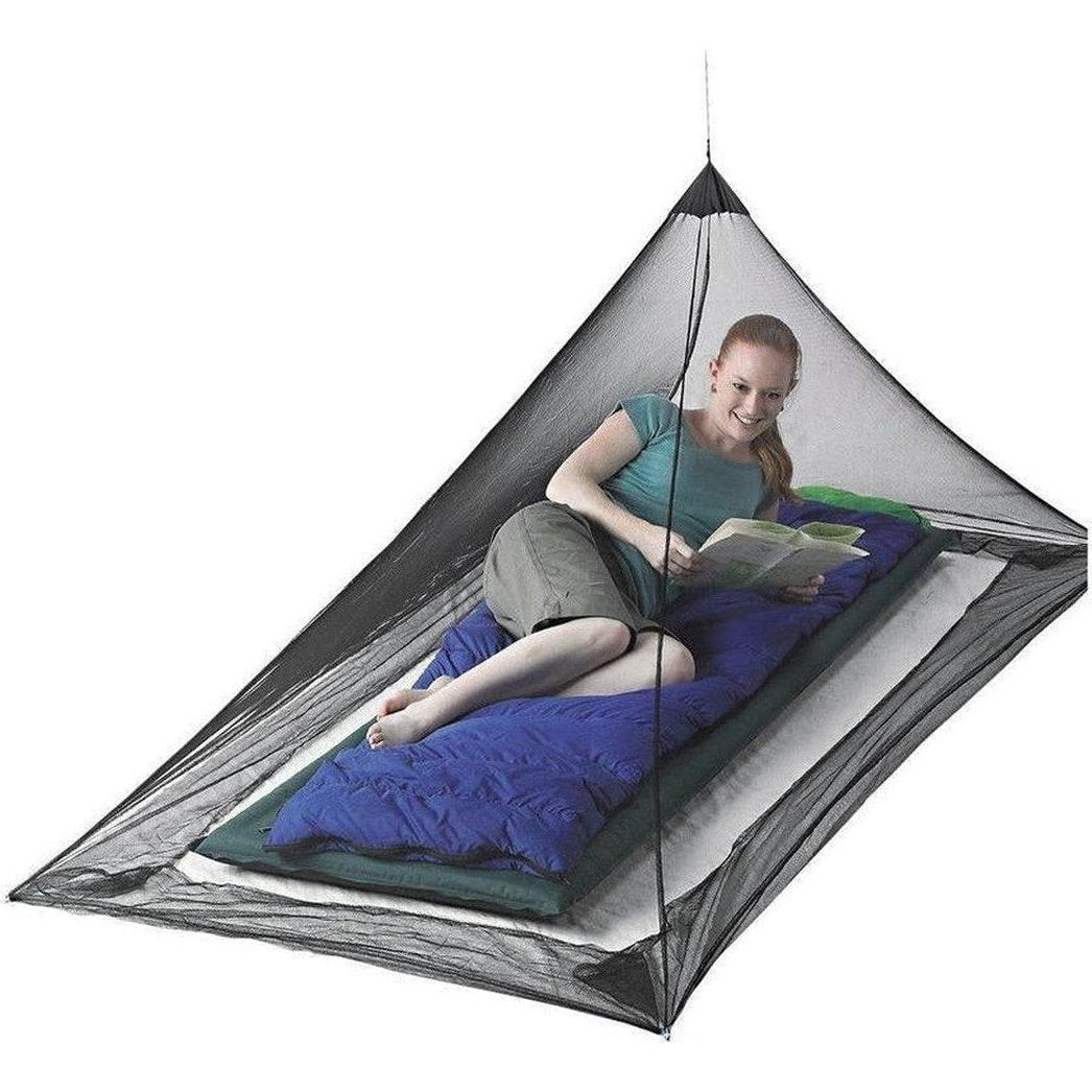 A woman reading on a blue sleeping pad inside a Sea To Summit Pyramid Net, showing the mesh design and camping setup.