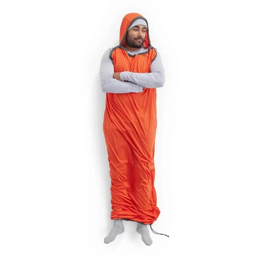 A man wearing the Sea To Summit Reactor Extreme Sleeping Bag Liner in orange stands with arms crossed against a white background.