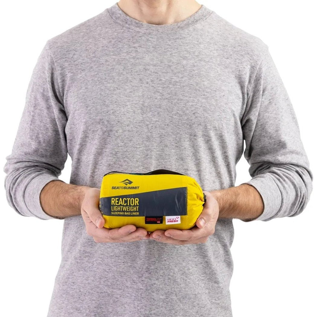 A man in a gray shirt holds the yellow Sea To Summit Reactor Lightweight Liner in front of a white background.