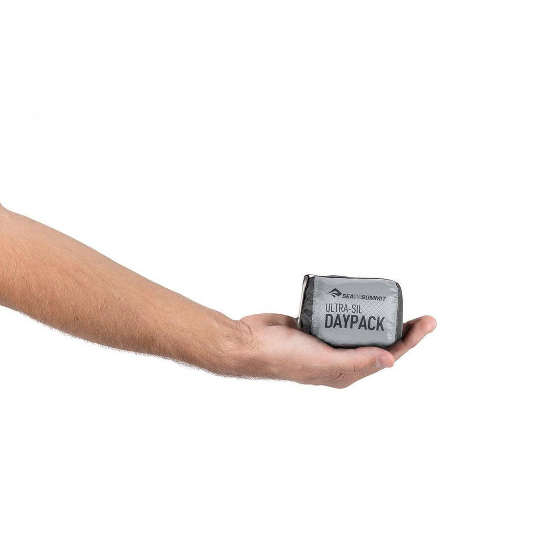 A hand holds the compact Sea To Summit Ultra-Sil Day Pack against a plain white background.