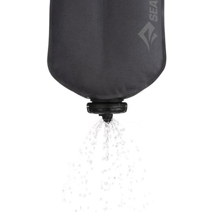 A charcoal Sea To Summit Watercell X hydration bladder pouring water against a white background.