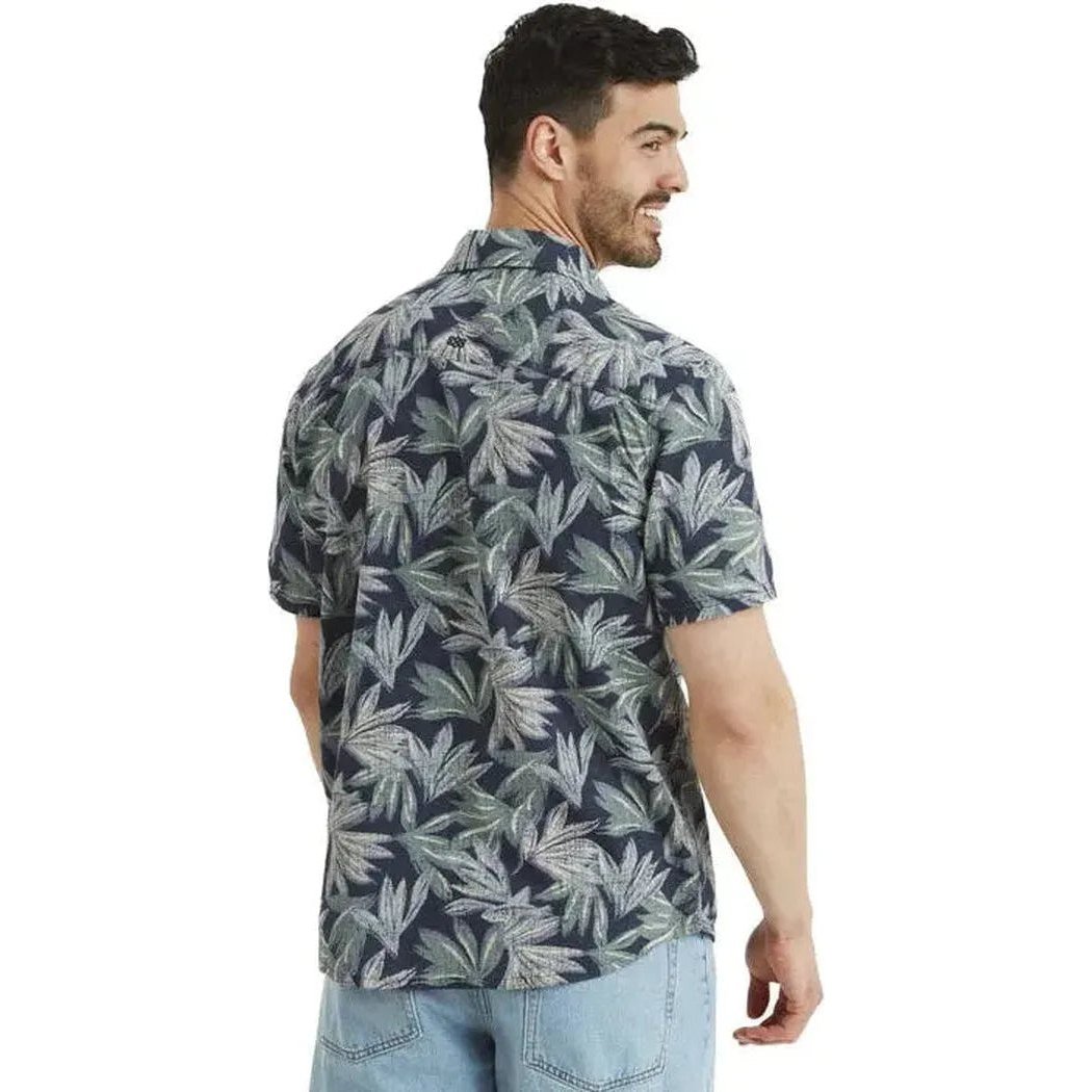 Back view of the Sherpa Adventure Gear Men's Havai Short Sleeve Shirt in Rathee Blue on a model wearing light blue jeans against a white background.