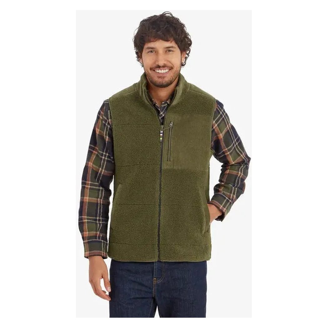 A front view of the Sherpa Adventure Gear Men's Rangeil Vest in Evergreen on a model wearing a plaid shirt and jeans against a white background.