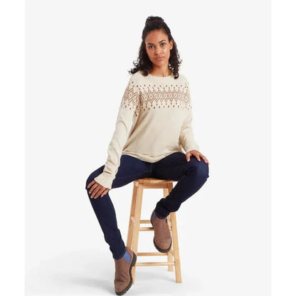 A woman sits on a wooden stool wearing the Sherpa Adventure Gear Samples - Women's Yeshe Crew Neck Sweater in Ecru against a white background.