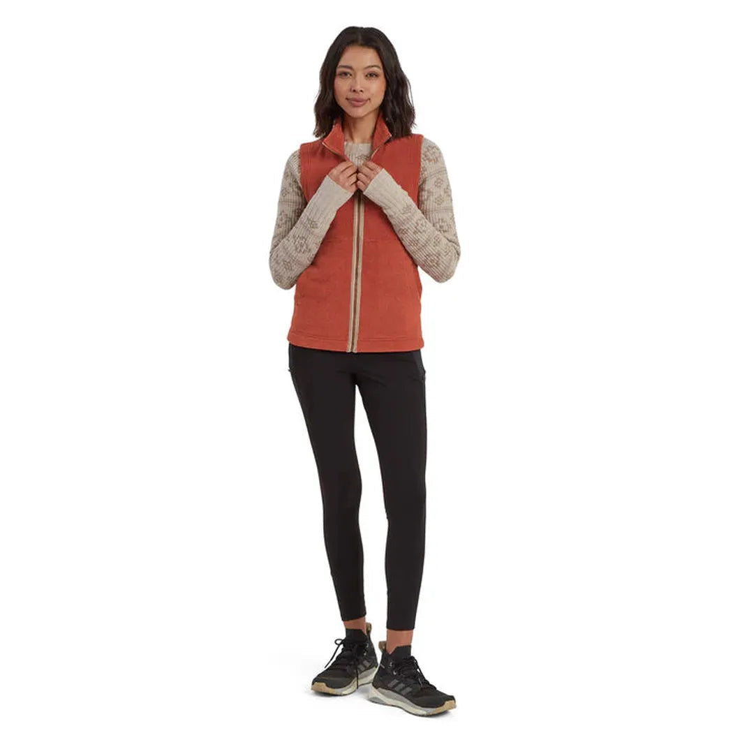 A woman wearing the Sherpa Adventure Gear Women's Rolpa Eco Vest in Rust stands against a white background.