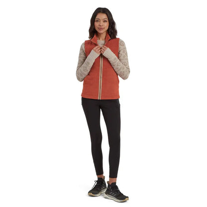 A woman wearing the Sherpa Adventure Gear Women's Rolpa Eco Vest in Rust stands against a white background.
