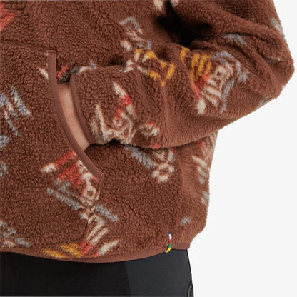 A close-up of the Sherpa Adventure Gear Women's Uddesya Eco 1/4 Zip in Cappuccino Yathra, showing the front pocket and a colorful tag on the hem against a white background.