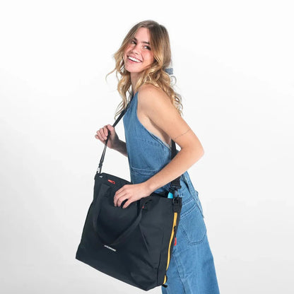 A woman in blue overalls carries the Sherpani Jetsetter Tote in Chromatic against a white background.