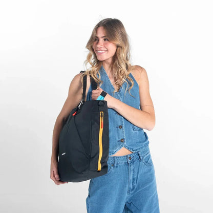 A woman wearing a denim top and jeans holds the Sherpani Jetsetter Tote in Chromatic against a white background.