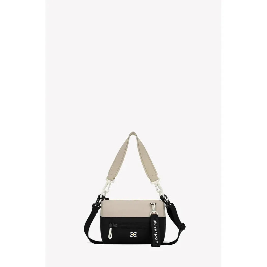 A front view of the Sherpani Skye bag in Alchemy color with a beige shoulder strap and black bottom section, showing a small logo and a tag, against a plain white background.