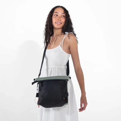 A woman in a white dress wears the Sherpani Vale AT bag in Aloe Mist, shown from the front against a plain white background.