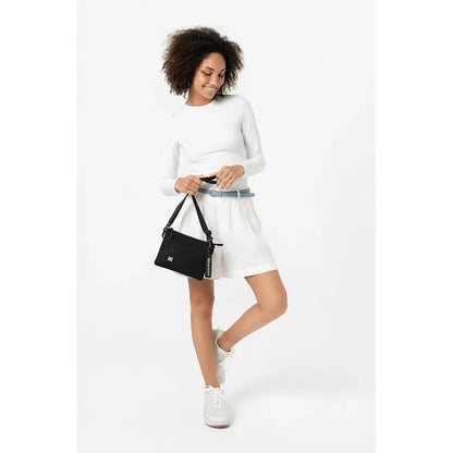 A model wearing a white dress and white sneakers holds the Sherpani Zoom bag in Con Leche against a white background.