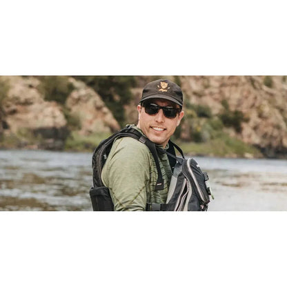 A man wearing the Shwood Canby ACTV sunglasses smiles while standing by a river with rocky cliffs in the background.