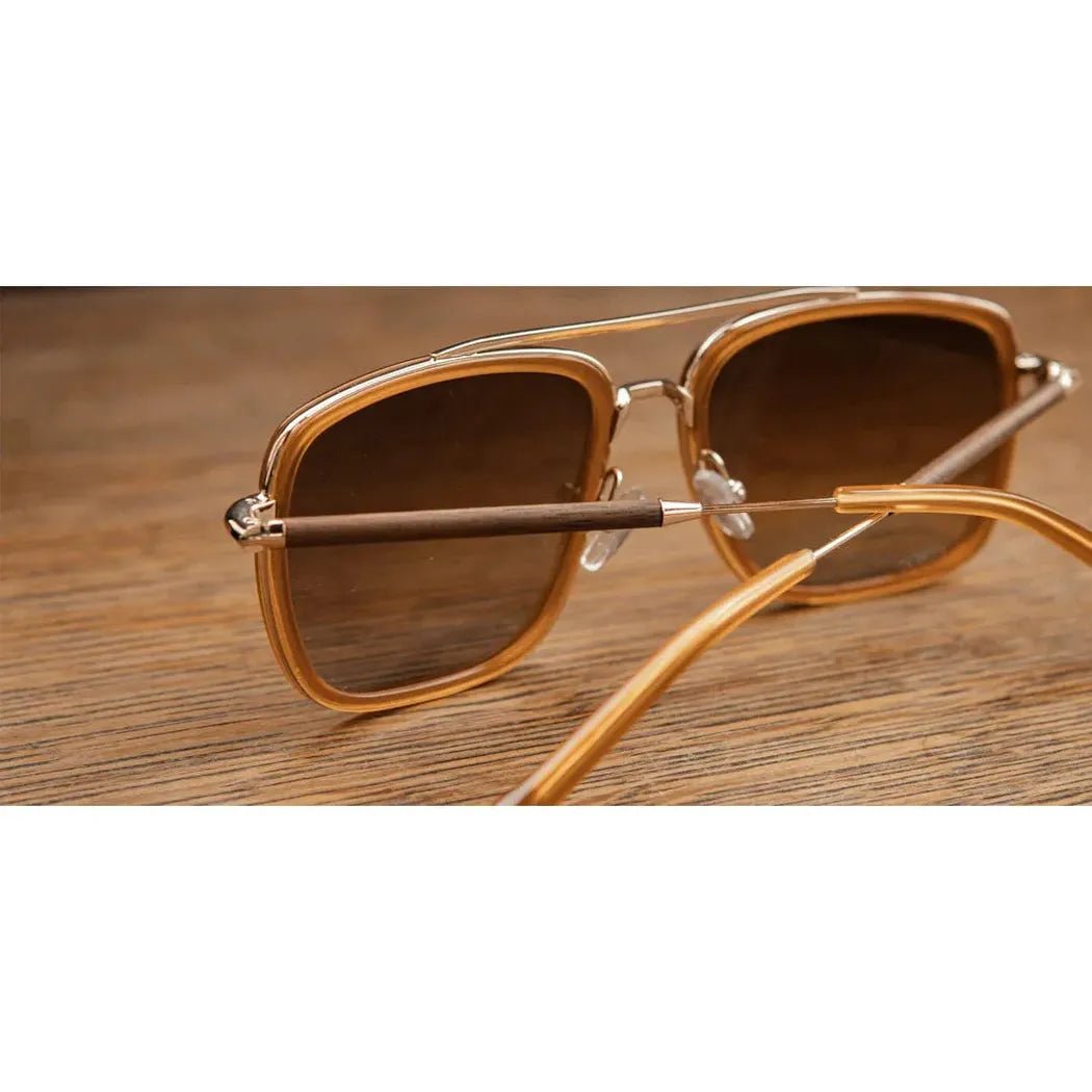Side view of the Shwood Grant sunglasses with caramel and gold frames and walnut arms on a wooden surface.