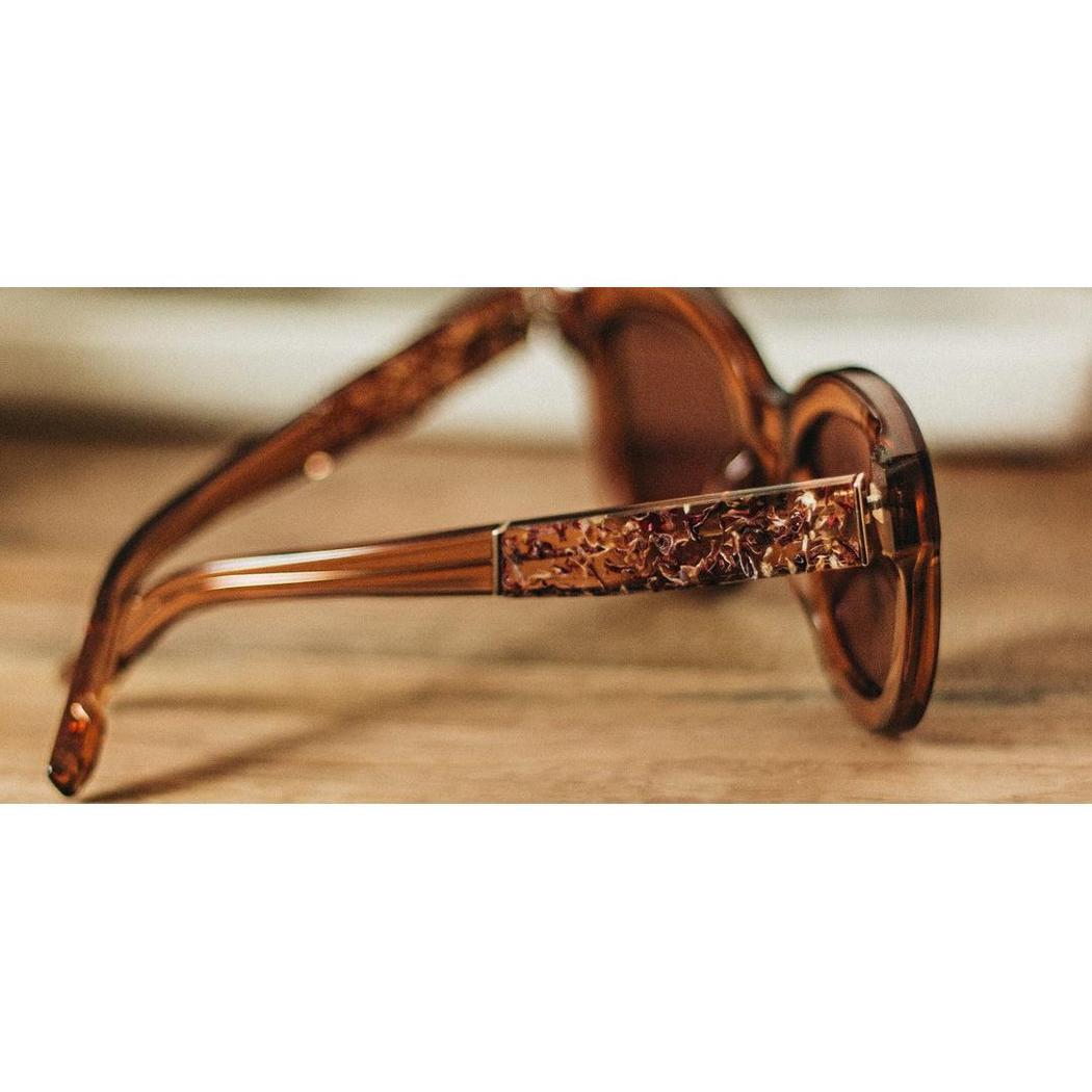Side view of the Shwood Lorane sunglasses with rose flower detail on the temple, set against a wooden surface.