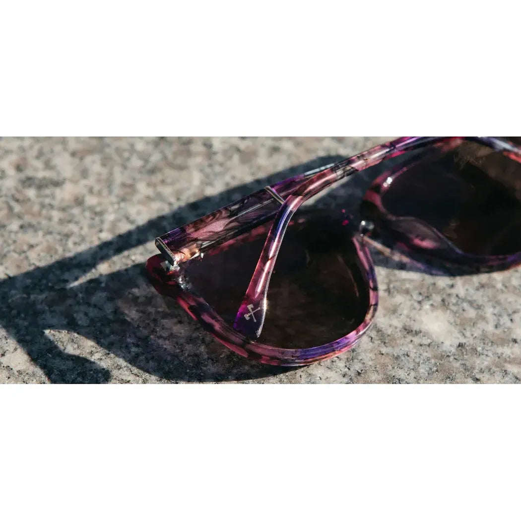 Close-up of the Shwood Mckenzie sunglasses in Amethyst on a textured stone surface.