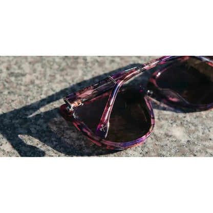 Close-up of the Shwood Mckenzie sunglasses in Amethyst on a textured stone surface.