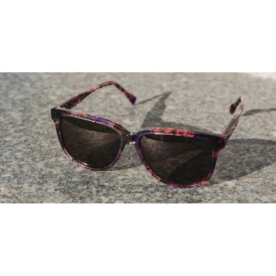 A front view of the Shwood Mckenzie Amethyst sunglasses on a gray stone surface.