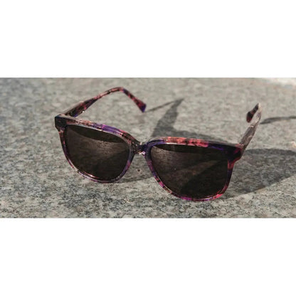 A front view of the Shwood Mckenzie Amethyst sunglasses on a gray stone surface.
