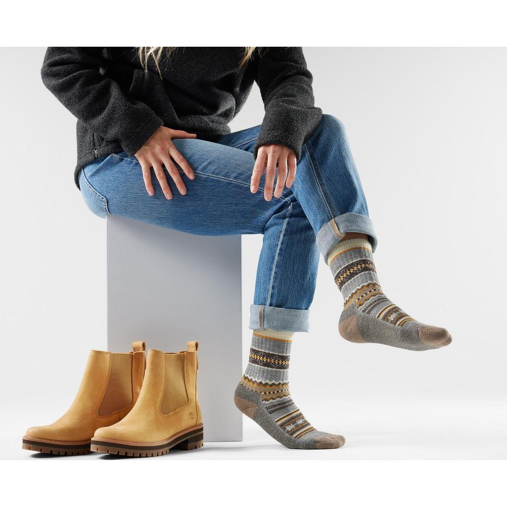 A model wearing Smartwool Everyday Cozy Snowed In Sweater Crew Socks in Garden Pink sits on a block with matching socks visible.