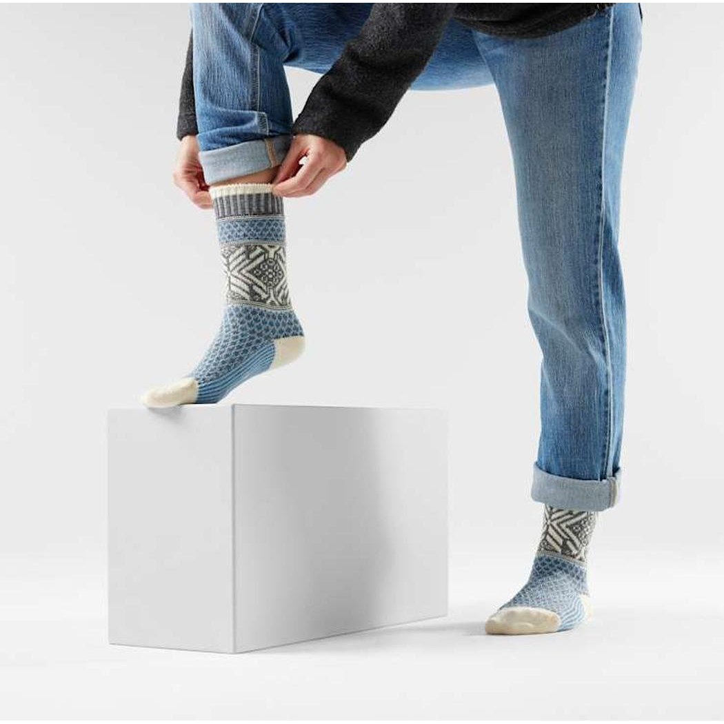 A model wearing Ash Smartwool Everyday Popcorn Snowflake Pattern Crew Socks adjusts one sock while standing on a white block.