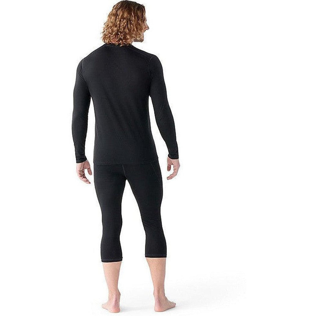 Back view of the Smartwool Men's Classic All-Season Merino Base Layer Long Sleeve in Black on a barefoot model against a white background.