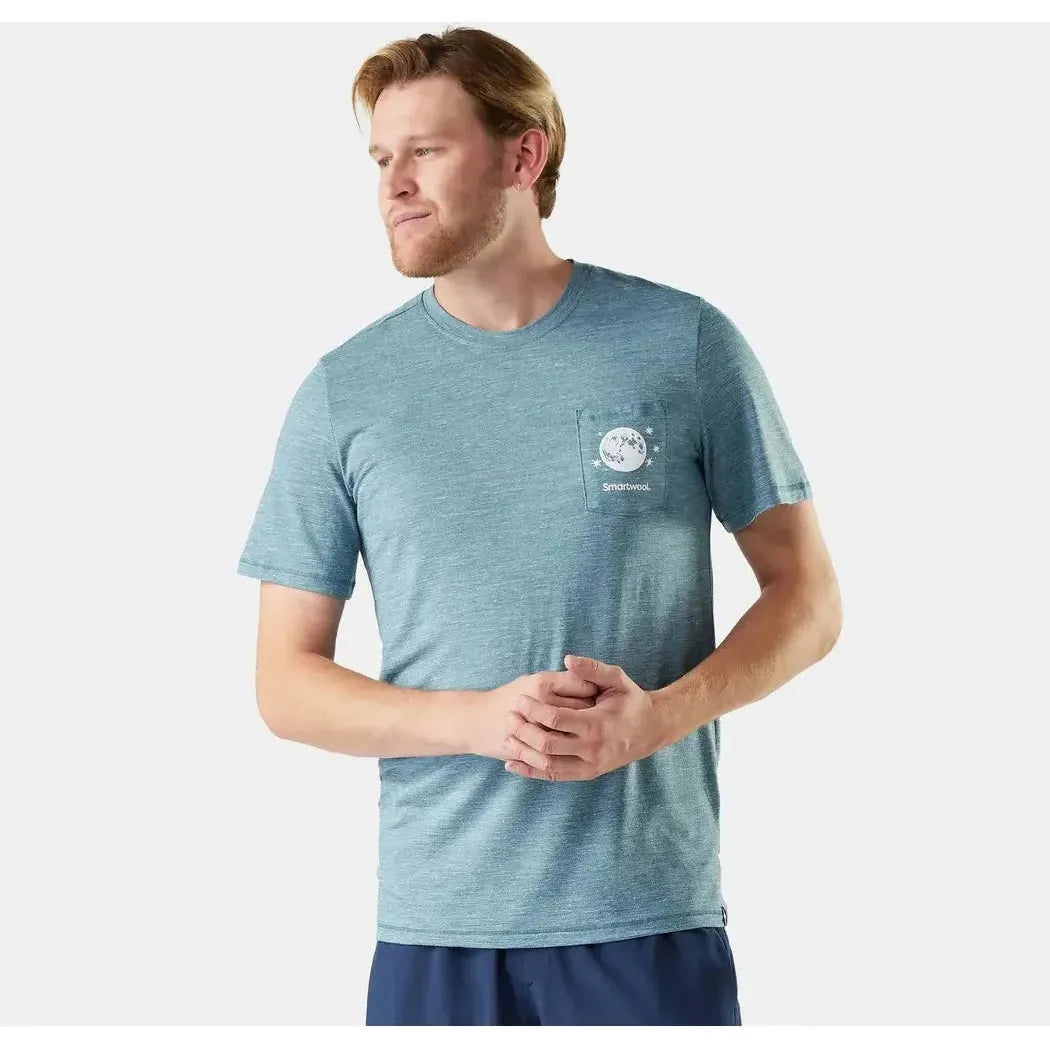 A man wears the Smartwool Men's Merino Hemp Blend Peak Pints Short Sleeve Graphic Tee in Dusty Teal, shown from the side against a plain white background.