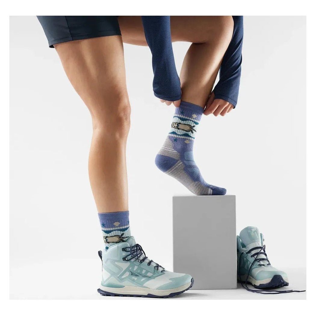 A woman adjusts her Ash Smartwool Women's Hike Light Cushion Otter Float Crew Socks while wearing light blue hiking boots on a white background.