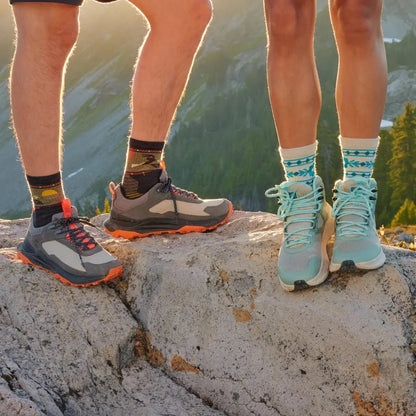 Two people stand on a rock with the woman wearing Moonbeam Smartwool Women's Hike Light Cushion Retro Floral Mid Crew Socks and light blue hiking shoes.