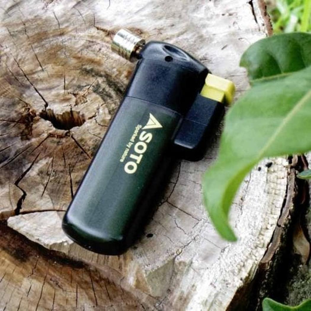 A black Soto Outdoors Pocket Torch rests on a tree stump with a green leaf nearby.