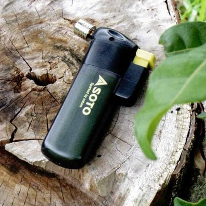 A black Soto Outdoors Pocket Torch rests on a tree stump with a green leaf nearby.