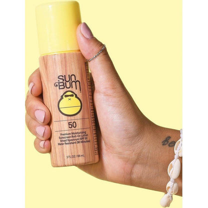 A hand holds a yellow-capped Sun Bum SPF 50 Original Roller Ball against a yellow background.