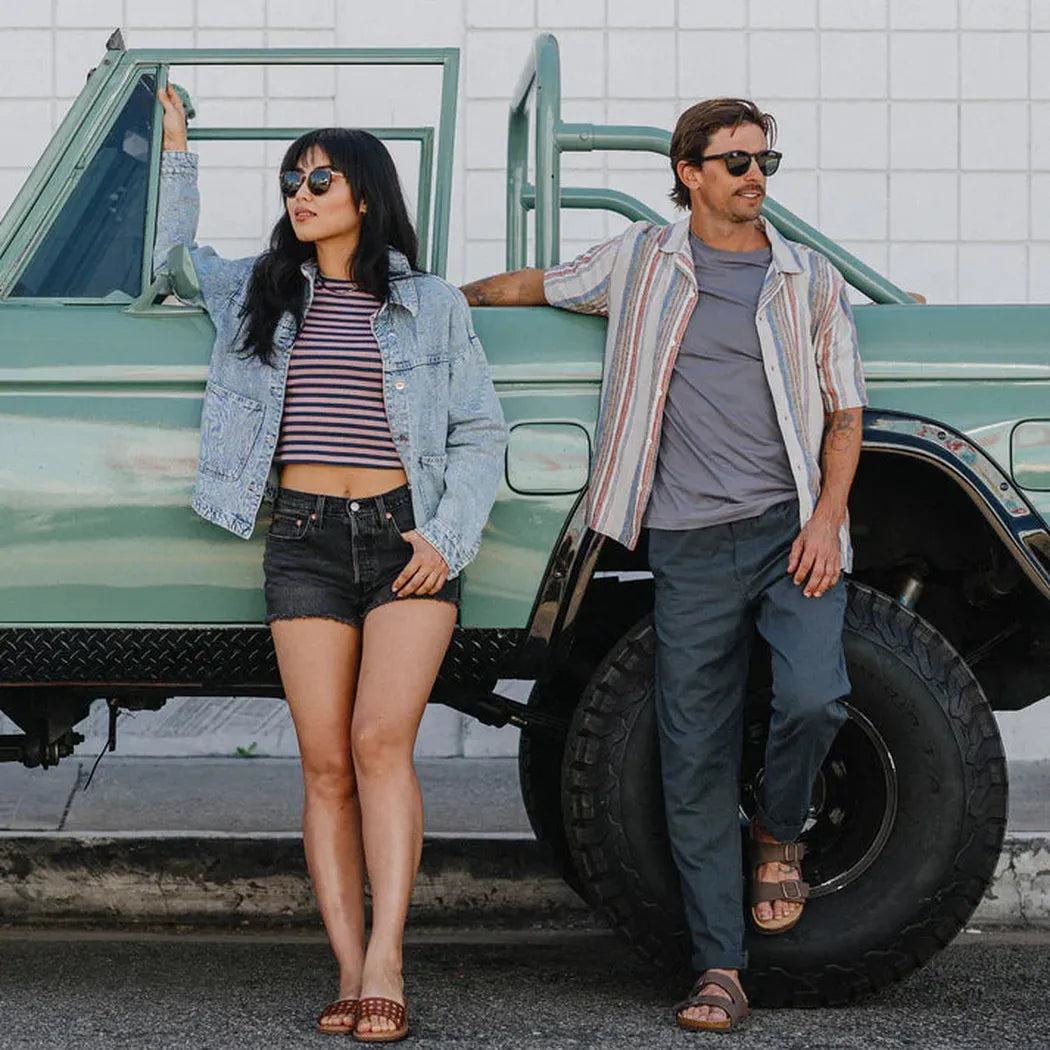 A woman and man in sunglasses stand by a green truck, wearing the Suncloud Barnes Matte Black sunglasses.
