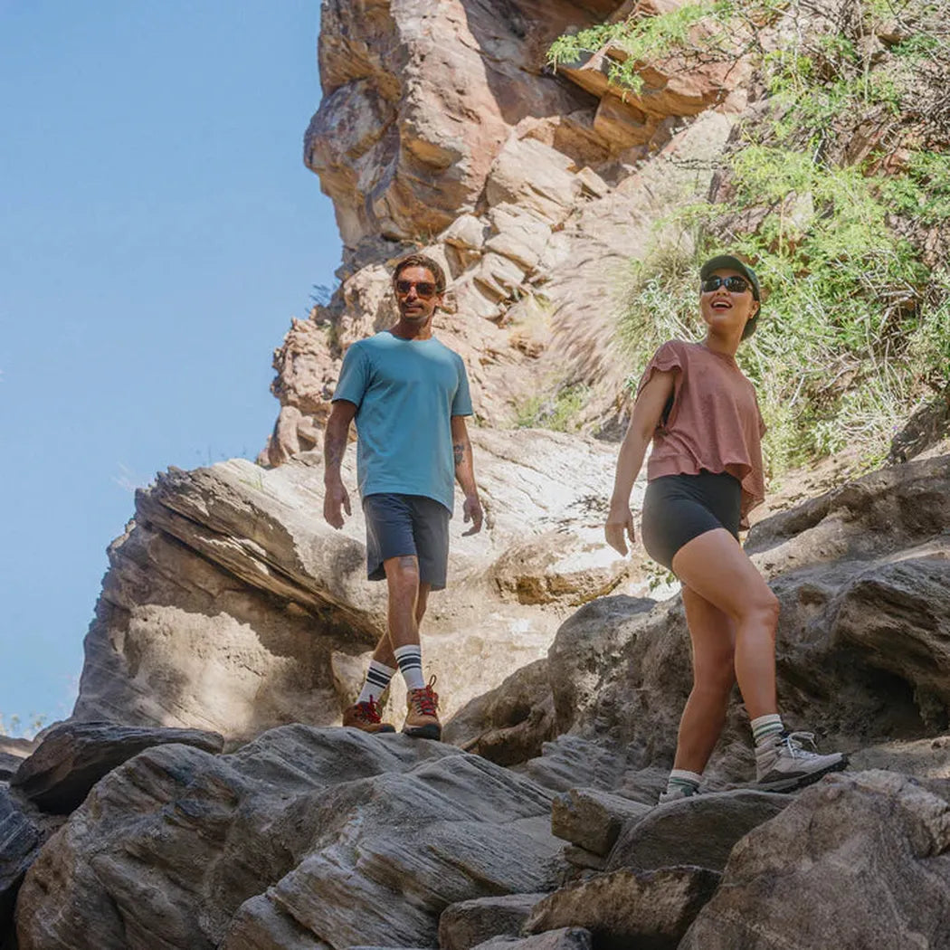 A man and woman hike on rocky terrain wearing Suncloud Sculpin Matte Black sunglasses.