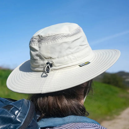 Back view of the Sunday Afternoons Cruiser Hat in Cream/Sand, showing the wide brim and a model wearing it against a blue sky and green landscape.