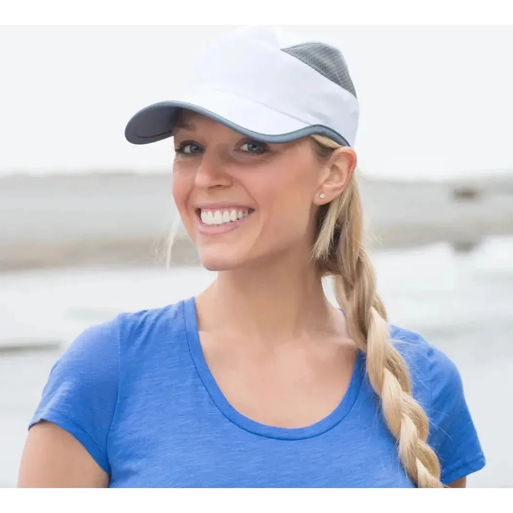 A woman wearing the Sunday Afternoons Eclipse Cap in Bluestone smiles at the camera with a beach background.