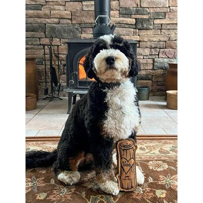 A black and white dog sits on a rug with a Tall Tails Natural Leather & Wool Love My Dog Log toy in front of a stone fireplace.