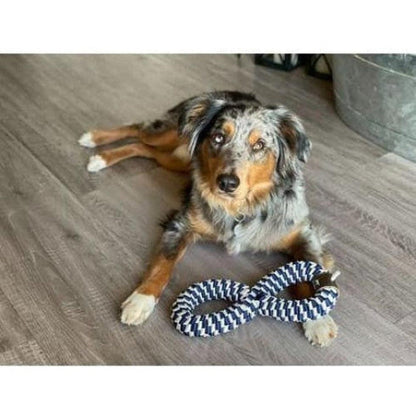 A dog lies on a wood floor with a Tall Tails Navy Braider Infinity Tug Toy in front of it.