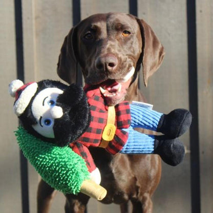 A brown dog holds the Tall Tails Paul Bunyan Rope Body Dog Toy in front of a metal fence.