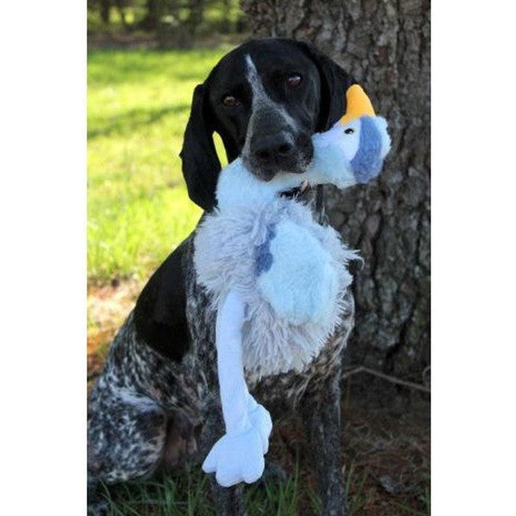 A black and gray dog sits outdoors holding the Tall Tails Plush Rope Body Heron Squeaker Toy against a tree.